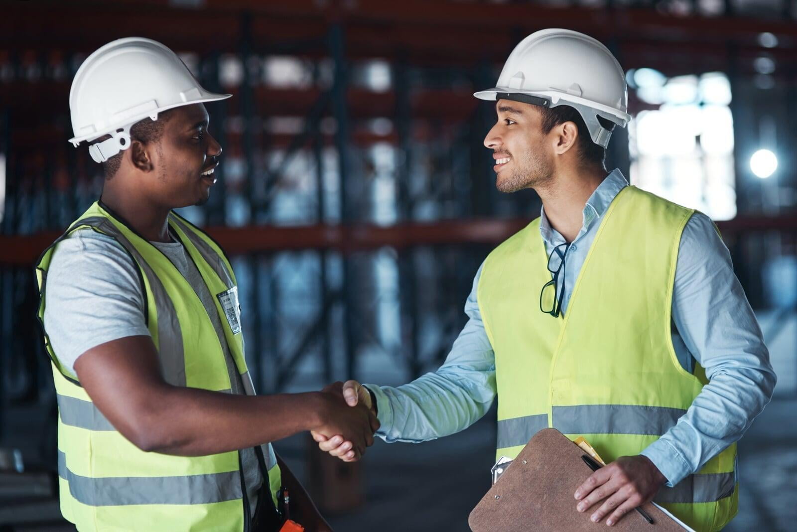 two men in wearing white hard hats and safety uniform in a construction site shaking hands